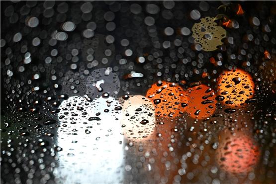 Lichter von Fahrzeugen scheinen durch eine Autoscheibe, die mit Regentropfen bedeckt ist. Foto: Bernd Weißbrod/dpa