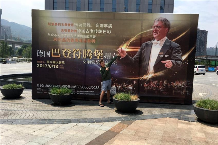 Zwei Empfinger im Reich der Mitte: Yanick Scholl vor dem Plakat seines Vaters, des Dirigenten Toni Scholl, in China. Privatbild
