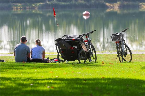 Ein Mann und eine Frau sitzen neben ihren Fahrrädern an einem See in Ertingen in der Sonne. Foto: Thomas Warnack/dpa/Symbolbild