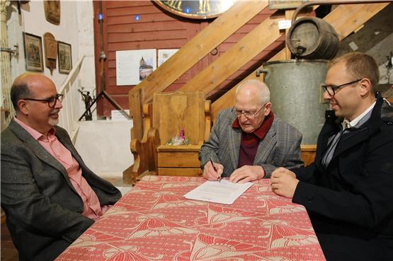 Erhard Schweizer junior (Mitte) unterschreibt im Beisein von Stefanus Schweizer (links) und Bürgermeister Ferdinand Truffner die Schenkungsurkunde. Bild Emil Henger