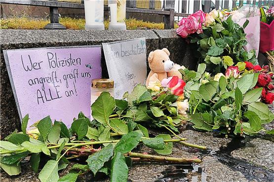 Kerzen und Blumen stehen am Tatort auf dem Marktplatz neben einem Schild „Wer Polizisten angreift, greift uns alle an!“. Foto: Dieter Leder/dpa