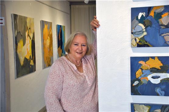Künstlerin Sylvia Grauer in der Galerie neben ihrer Bildanordnung „Serie Blau“: Auf einer Fläche von dreißig Mal dreißig Zentimeter gibt es Farbspiele aus aufgehelltem Indigoblau und der Komplementärfarbe Orange. Bild: Jana Breuling