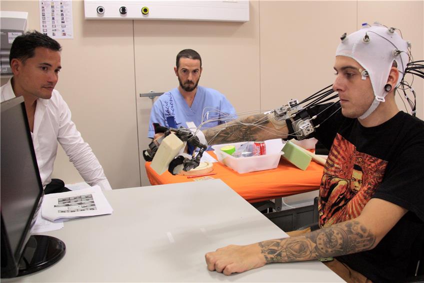 Surjo Soekadar (links) beobachtet, wie ein Patient mit seiner robotergeführten Hand ein Holzstück greift. Bild: Soekadar/Universität Tübingen